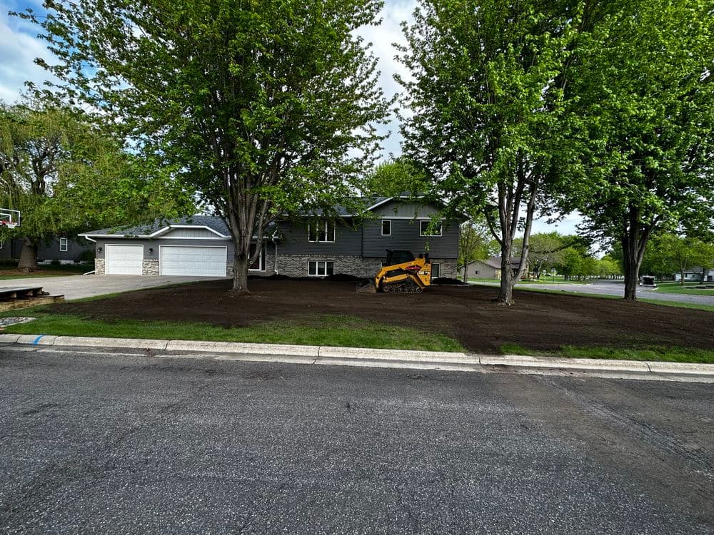 Home renovation with fresh landscaping and a mini excavator parked on treated lawn area.