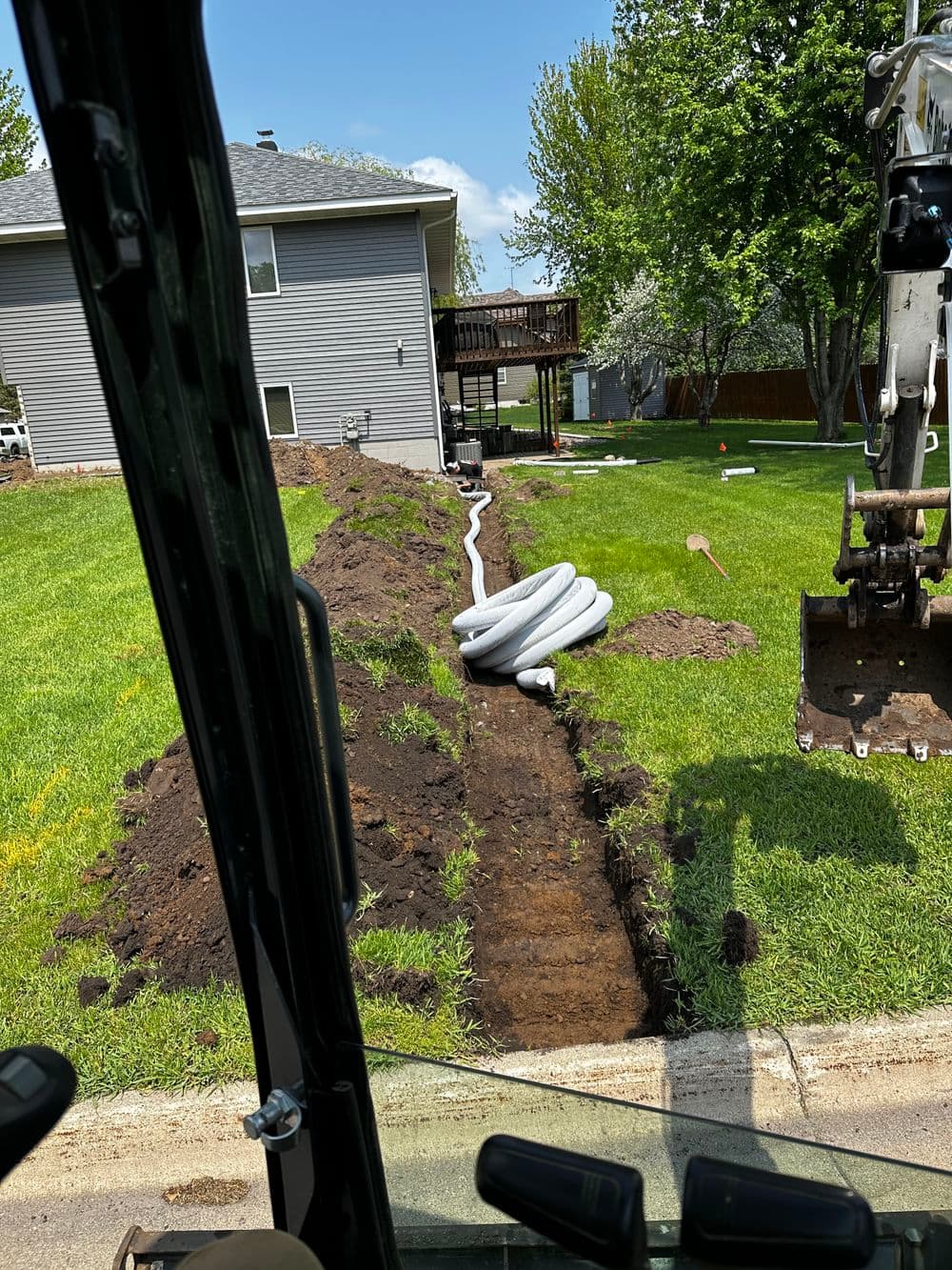 Excavation view showing installed piping in a residential yard under blue sky.