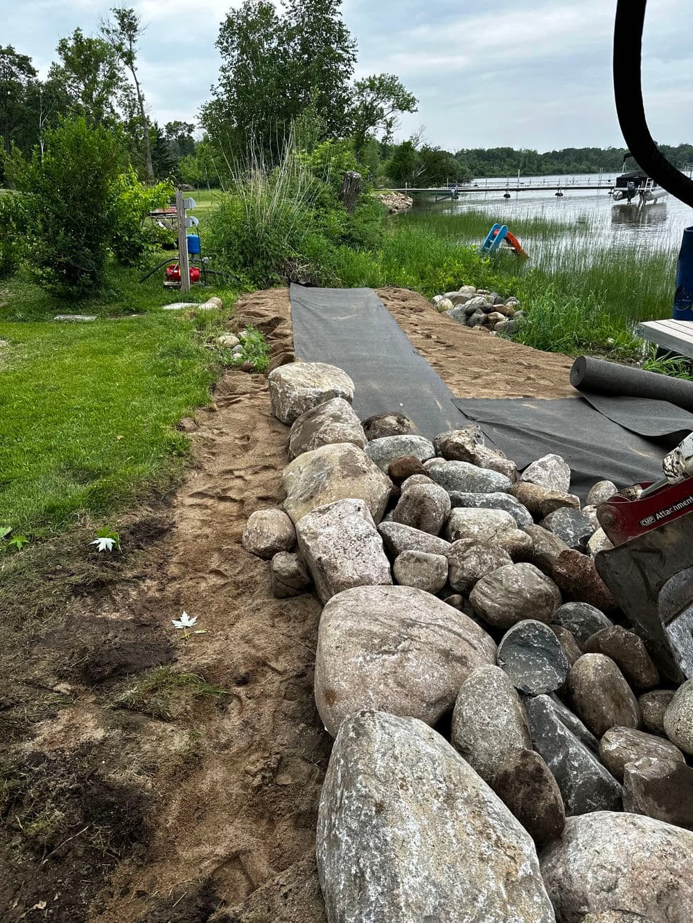 Landscape featuring a rocky path alongside a lake, with grass and trees in the background.