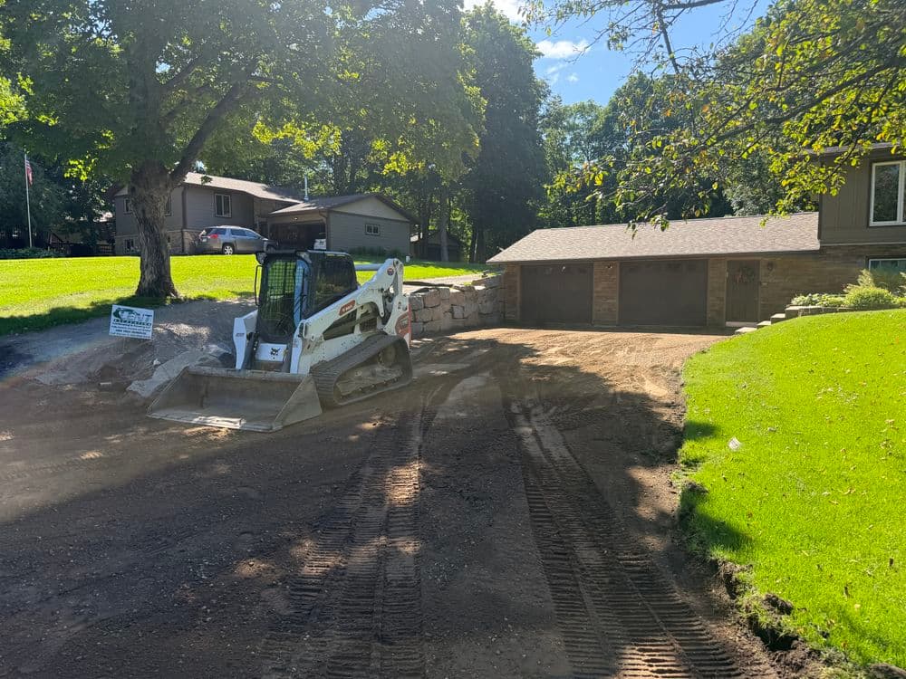 Bobcat skid steer loader working on a residential landscaping project near a garage.