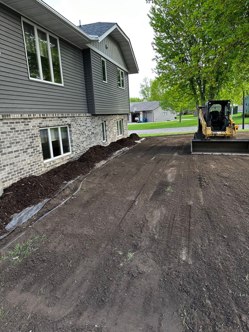 Exterior home landscaping with freshly leveled soil and mulch near a construction vehicle.