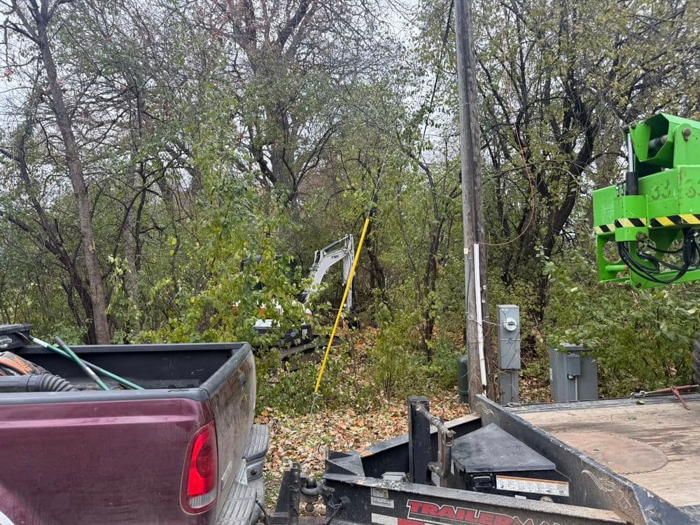 Utility truck near overgrown trees with power equipment visible in a rural area.